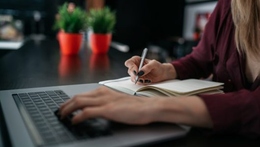 Female hand writing on notebook using pencil notebook at coffee shop. Request for online search in Internet while writing notes in a notebook using modern netbook computer connected to wireless.